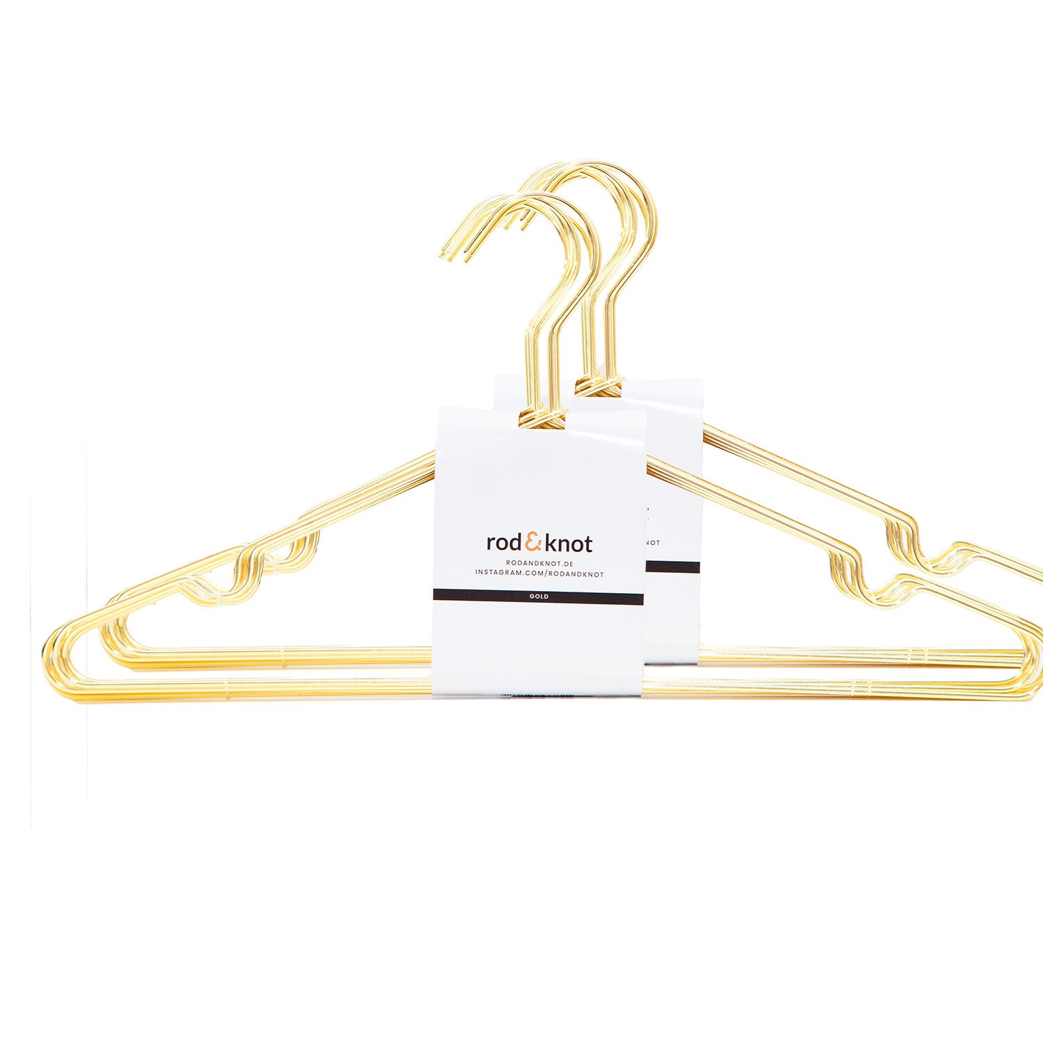 Drei Kleiderbügel von „rod & knot“, aus stabilem Metall und mit glänzendem Goldfinish, sind übereinander gestapelt und teilweise mit einem weißen Papieretikett umwickelt. Diese „Kleiderbügel aus stabilem Metall (Bundles)“ eignen sich perfekt zur platzsparenden Aufbewahrung, abgebildet vor weißem Hintergrund.