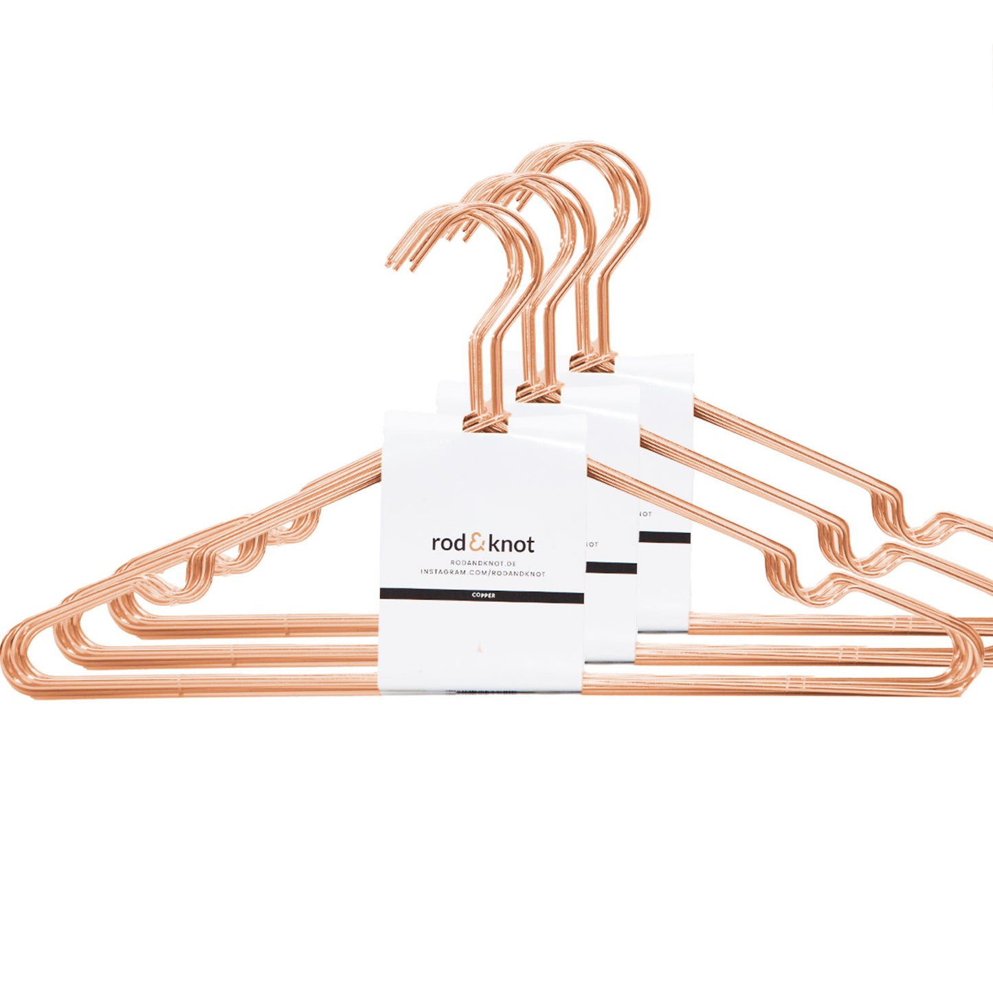 Ein Satz kupferfarbener Kleiderbügel aus stabilem Metall der Marke „rod & knot“, in einer Gruppe angeordnet. Die Kleiderbügel sind zusammen mit einer weißen Papierverpackung gebündelt, auf der das Logo und der Name der Marke in schwarzer und orangefarbener Schrift zu sehen sind. Der Hintergrund ist schlicht weiß und betont die platzsparende Aufbewahrung.