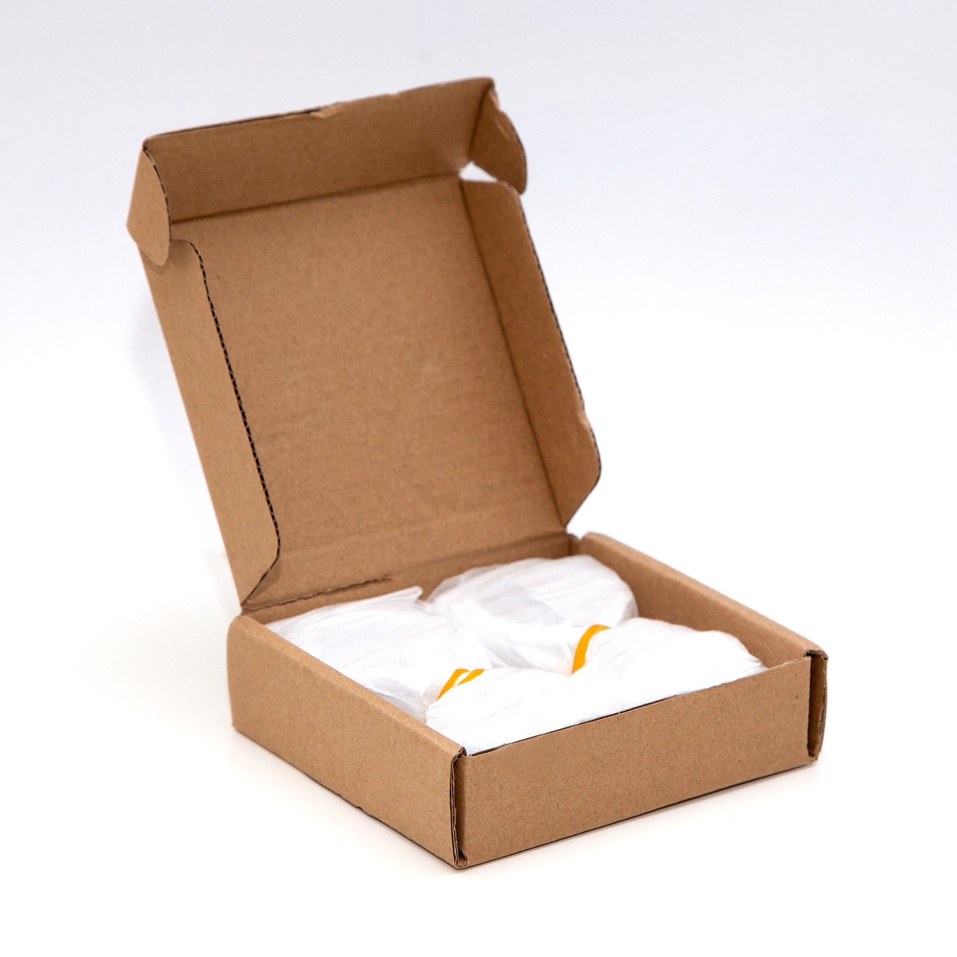 Eine kleine, offene Pappschachtel mit zwei verpackten Artikeln darin. Die Artikel sind in weißes Seidenpapier eingewickelt, wobei durch die Verpackung ein Hauch von Orange sichtbar ist, und mit zierlichen S-Haken aus stabilem Metall (8 Stück) von Rod & Knot gesichert. Die Schachtel steht vor einem schlichten weißen Hintergrund.